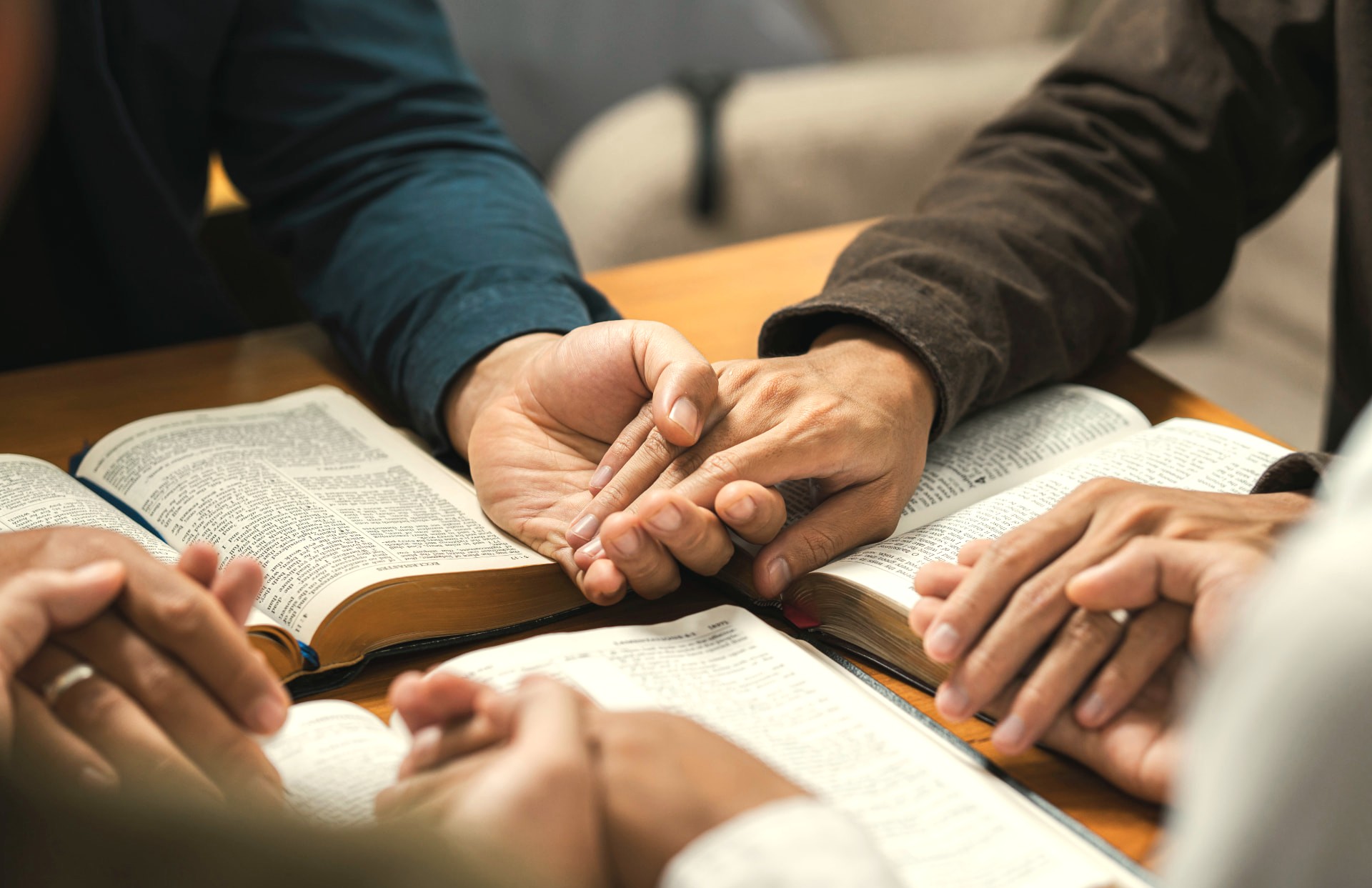 Members holding hands in prayer over open Bibles on a table