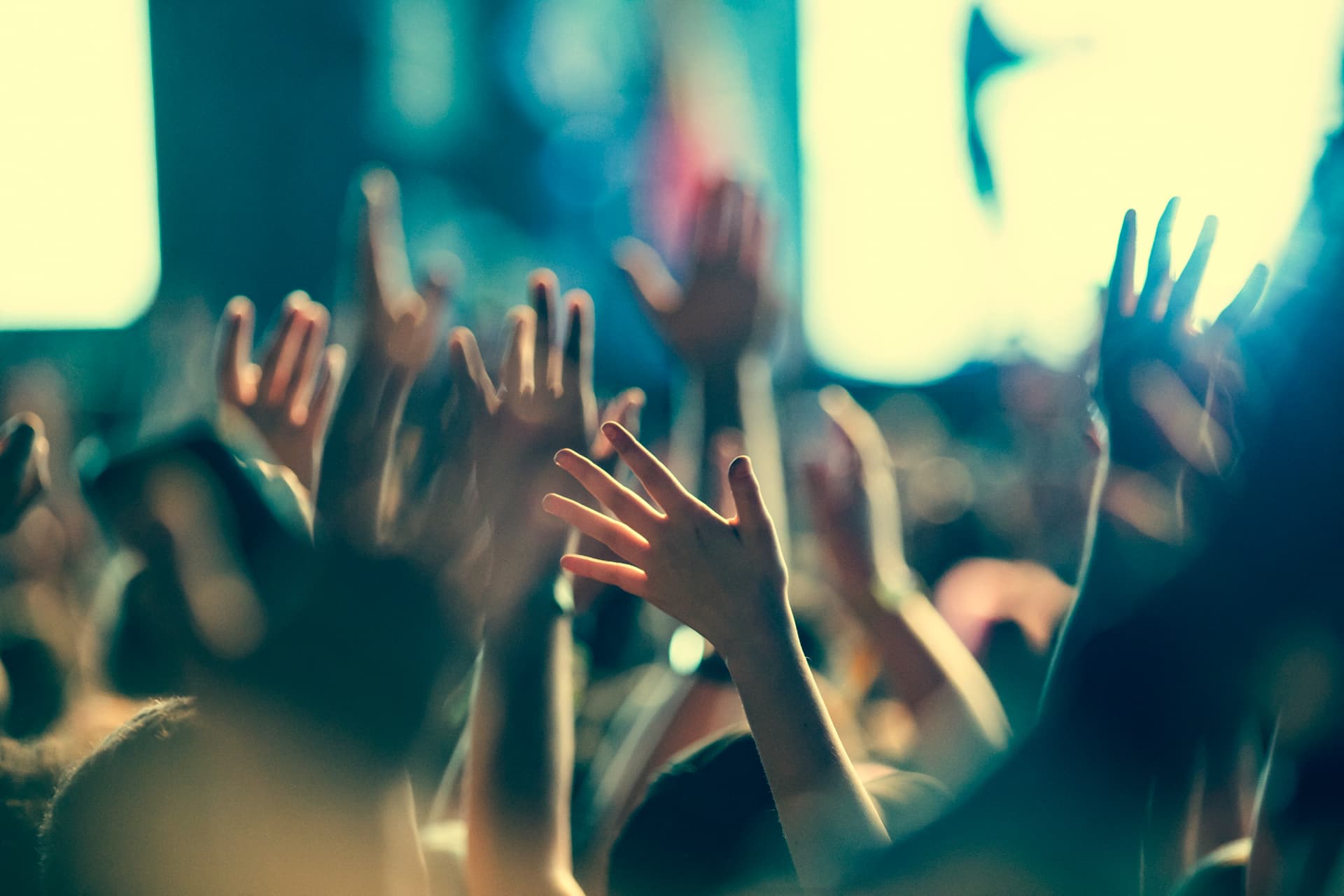 A crowd with hands raised toward a brightly lit stage